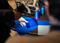 A person wearing a white glove uses a handheld device to scan a blue fabric swatch—an elegant step in configuring bespoke interiors, reminiscent of the luxury experience behind the Bugatti Tourbillon.