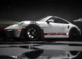 A white Porsche 911 GT3 RS with red decals and a large rear wing is parked indoors on a reflective floor at the Porsche Experience Center, captured in dramatic lighting.