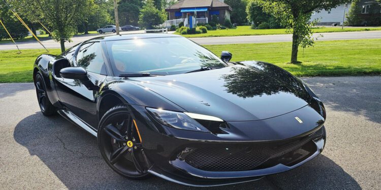 A sleek black Ferrari 296 GTB sports car is parked on a paved driveway, enjoying the Royal Treatment from WrapKings, with trees, grass, and houses in the background on a sunny day.