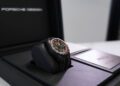 A Porsche Design wristwatch with a black band and red accents is displayed in an open black box with Porsche Design branding—an ideal accessory for enthusiasts of the 911 GT3 RS or visitors to the Porsche Experience Center.