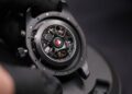 A gloved hand holds the back of a black mechanical wristwatch, showing exposed gears and intricate inner workings—much like the engineering marvels seen at the Porsche Experience Center.