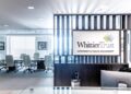 Modern office reception area with a sign reading "Whittier Trust Wealth Management" and a glass-walled conference room with white chairs in the background.