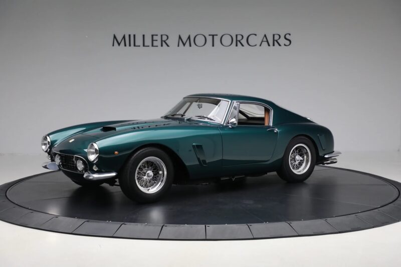 A classic green vintage Ferrari sports car is displayed in a showroom with "Miller Motorcars" signage in the background.