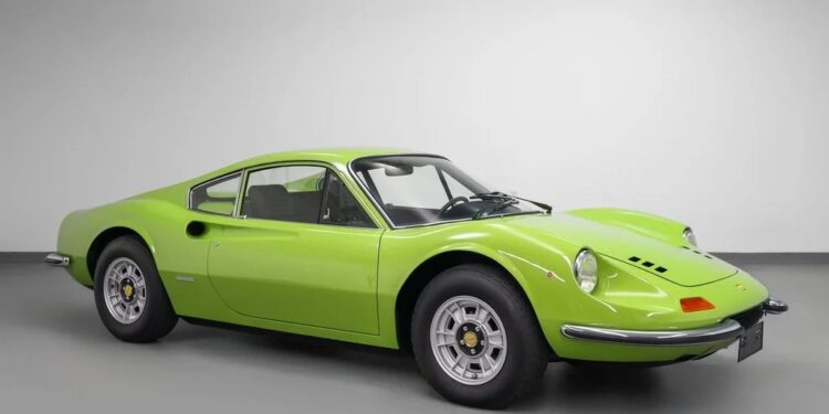 A classic lime green Ferrari sports car, likely from the 1970s, is parked in a plain white indoor studio, viewed from the side at an angle—showcasing its striking colors and sleek design, now available for sale.