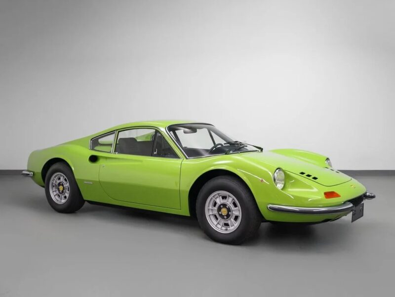 A classic lime green Ferrari sports car, likely from the 1970s, is parked in a plain white indoor studio, viewed from the side at an angle—showcasing its striking colors and sleek design, now available for sale.