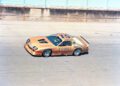 A gold race car with the number 15 and Budweiser logos drives on a racetrack at Laguna Seca during the Rolex Monterey Motorsports Reunion. The car also features "Elliott," "Goodyear," and IROC All-Star branding.