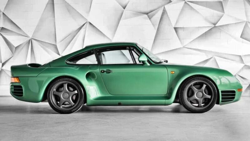 A green sports car, one of the best manual supercars, is parked indoors against a white geometric-patterned wall, shown in profile from the side—now for sale.