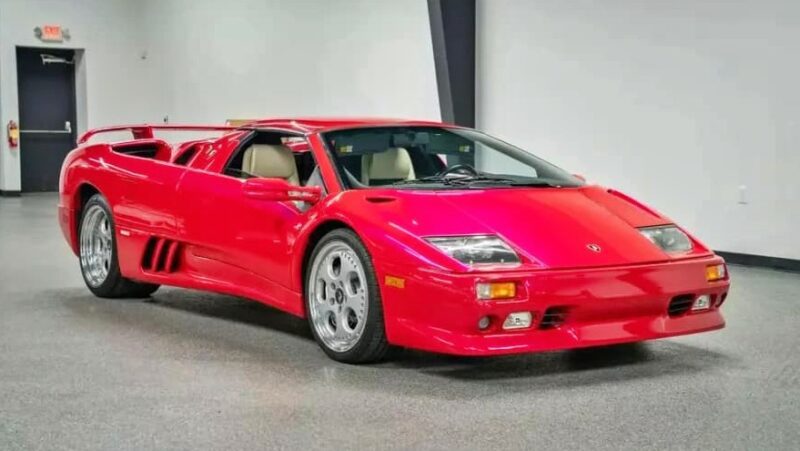 A red Lamborghini Diablo, one of the best manual supercars, is parked indoors on a gray floor with headlights off and the driver's door closed. For sale now.