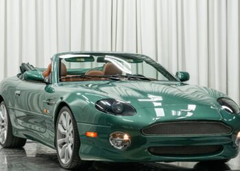 A green convertible sports car with the top down is parked indoors in front of white curtains, showcasing one of the classic automotive color combos often sought after by enthusiasts searching for standout cars for sale.