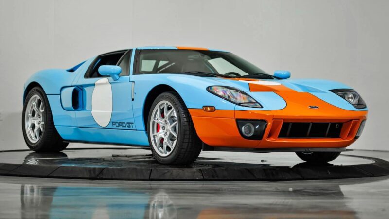 A blue and orange Ford GT sports car with racing decals, known as one of the best manual supercars, is displayed indoors on a circular platform.