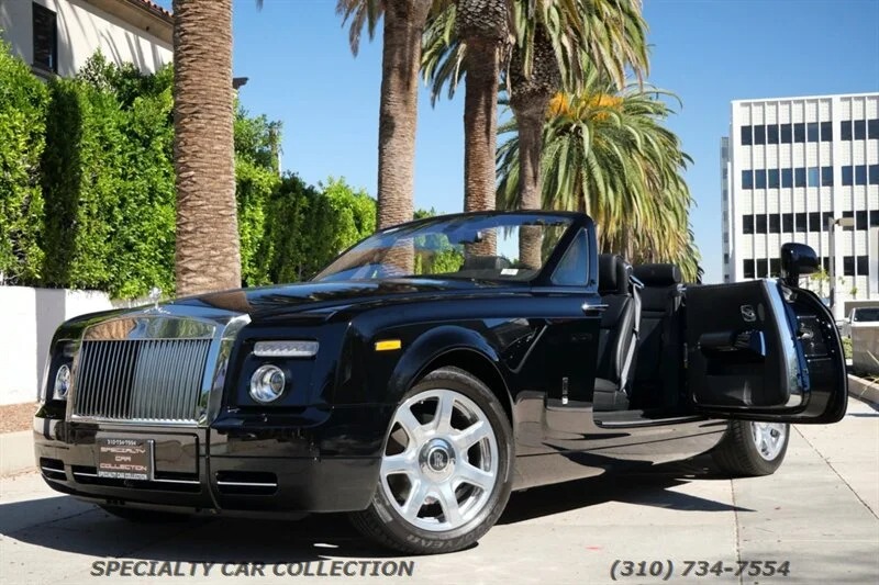 Juodojo „Rolls-Royce“ fantomo kabrioletas su atidarytomis vairuotojo pusės durelėmis yra pastatytas saulėtoje gatvėje, išklotoje palmėmis ir komerciniais pastatais, įkūnijant esminę prabangaus sedano patirtį.