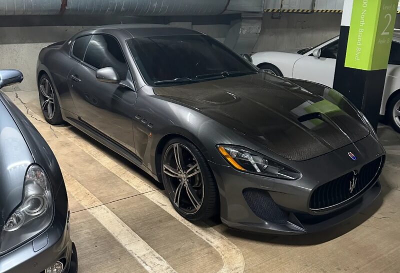 A grey Maserati, a symbol of Italian luxury, is parked in an indoor parking garage next to another vehicle.