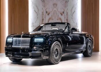 A black Rolls-Royce Phantom convertible, the epitome of a luxury car, is displayed indoors on a light floor with vertical wooden panels and marble walls as the elegant backdrop.