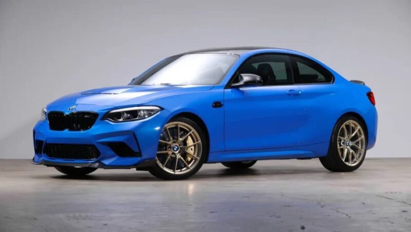 A blue two-door sports coupe, For Sale: Best Sports Car Under $100k, is parked indoors against a plain light gray background.