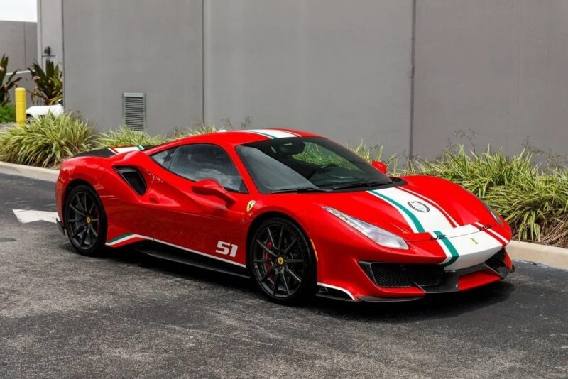 A track-ready Ferrari 488 Pista with white and green racing stripes and the number 51 is parked beside a gray building and some greenery.