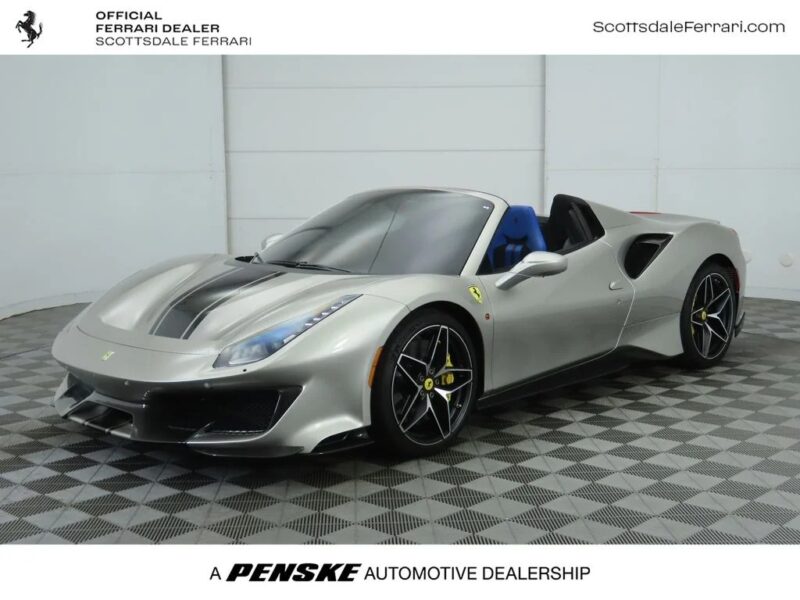 A silver Ferrari 488 Pista convertible with black racing stripes is displayed in a showroom with patterned flooring, highlighting its track-ready performance.