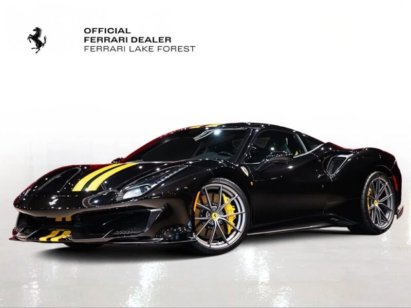 A track-ready Ferrari 488 Pista in black with yellow racing stripes is displayed in a showroom with a sign reading "Official Ferrari Dealer Ferrari Lake Forest." This stunning Ferrari for sale is sure to turn heads.