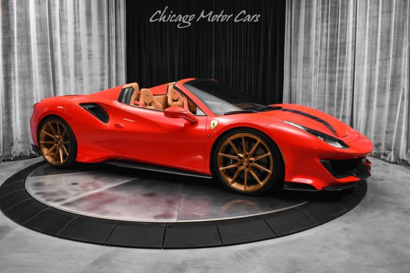 A red Ferrari 488 Pista convertible with bronze wheels is displayed on a rotating platform in front of curtains at Chicago Motor Cars, showcasing this track-ready Ferrari for sale.
