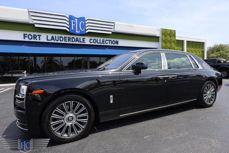 „Fort Loderdale“ kolekcijos prekybos atstovų pastato priešais „Fort Loderdale“ kolekcijos atstovų pastatą „Juodojo„ Rolls-Royce “phantomo prabangaus sedanas saulėtą dieną.