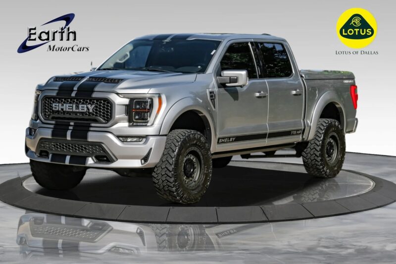 A silver Shelby Ford F-150 pickup truck is displayed on a turntable platform, showcasing Shelby trucks with Earth MotorCars and Lotus of Dallas logos in the background.