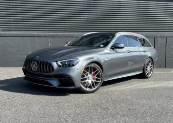 A silver Mercedes-Benz AMG station wagon, one of the finest luxury performance wagons, is parked on a paved surface in front of a dark industrial building.