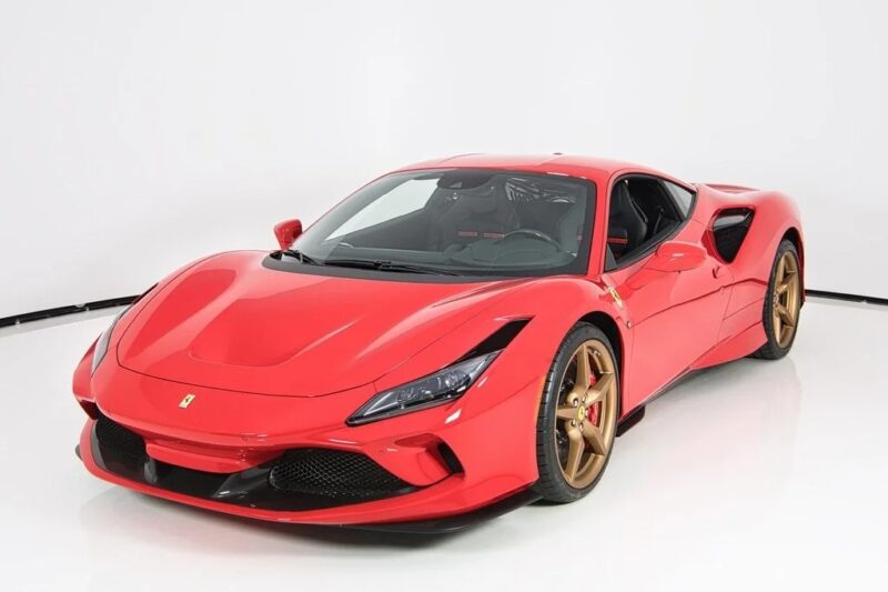 A red Ferrari sports car with bronze wheels is parked in a white studio setting, viewed from the front left angle—an exotic car for sale perfect for those seeking top car listings.