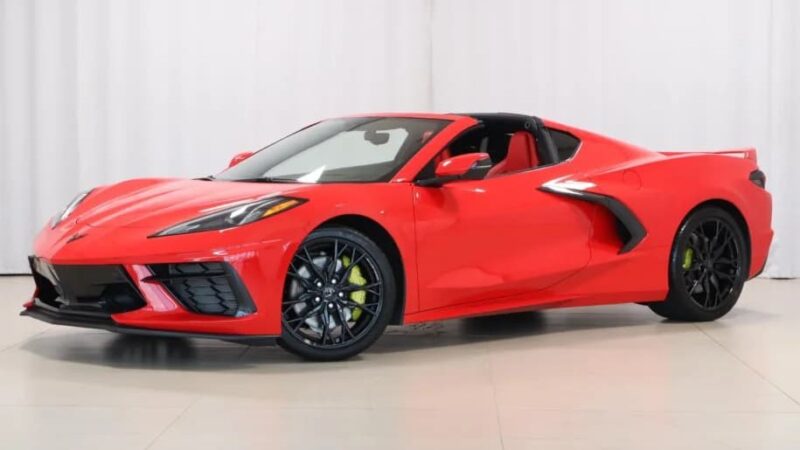 A red Chevrolet Corvette sports car with a black roof and wheels, parked indoors against a plain white background. For Sale: Best Sports Car Under $100k.
