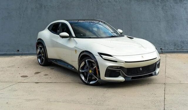 A white Ferrari Purosangue SUV is parked on a concrete surface in front of a gray wall, showcasing why it’s among the best Ferrari SUVs for sale.