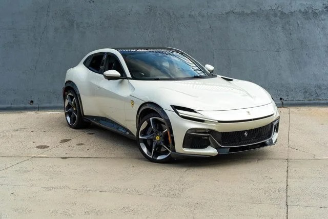 A white Ferrari Purosangue SUV is parked on a concrete surface in front of a gray wall, showcasing why it’s among the best Ferrari SUVs for sale.