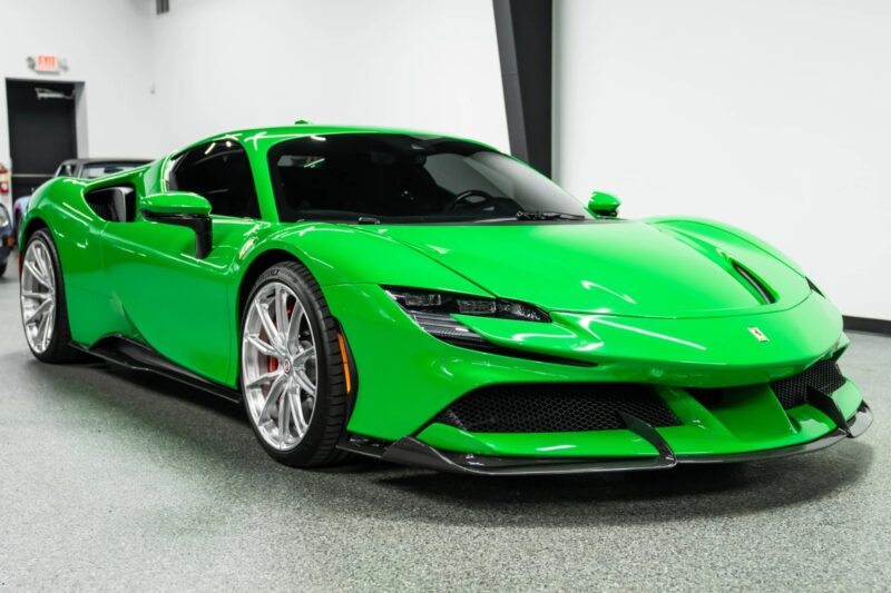 A bright green Ferrari, showcasing one of the bold Ferrari colors, is parked indoors on a speckled floor, with its front and side visible.
