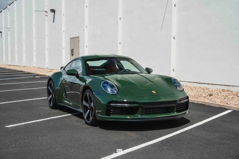 A green Porsche 911 Sport Classic is parked in an empty parking lot next to a white building, showcasing a timeless icon from Porsche history.