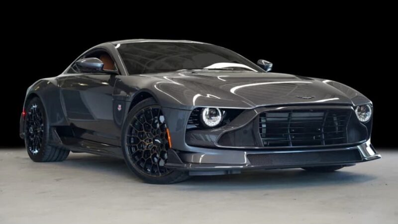 A matte black sports car with a wide body kit, black mesh wheels, and aggressive front styling, parked on a light concrete floor against a black background—one of the best manual supercars for sale.