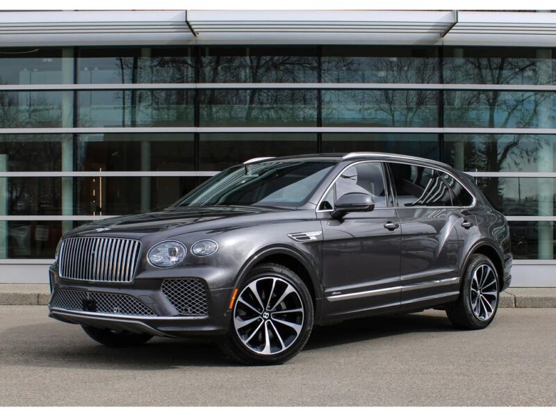 A gray luxury Bentley SUV parked in front of a modern glass building, viewed from the front-left angle—perfect for those seeking the best Bentleys for sale.