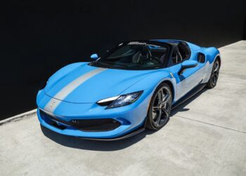 A blue Ferrari luxury car with a silver racing stripe is parked on a concrete surface next to a black wall.