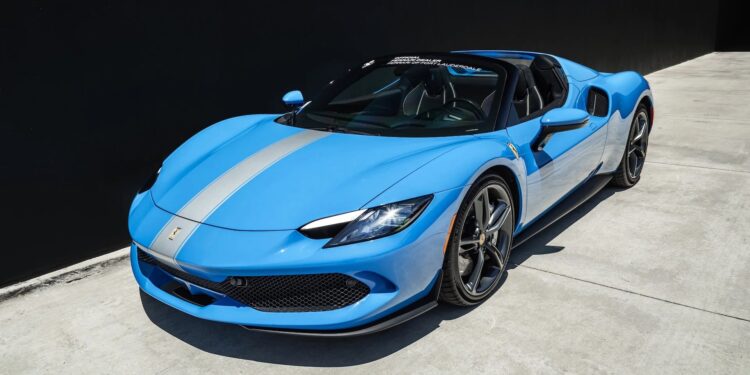 A blue Ferrari luxury car with a silver racing stripe is parked on a concrete surface next to a black wall.