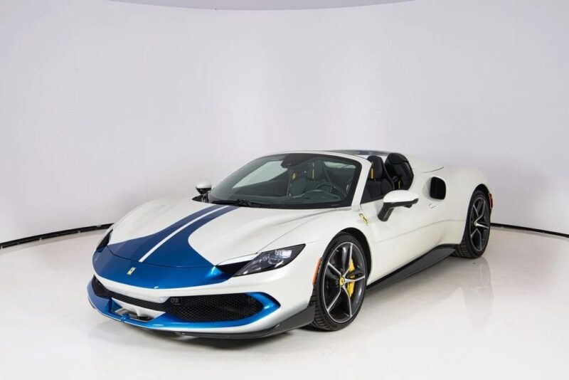 A white Ferrari convertible sports car with blue racing stripes and yellow brake calipers is parked in a white studio setting, showcasing some of the most striking Ferrari colors for sale.