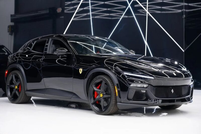 A black Ferrari Purosangue with red brake calipers is parked indoors on a white floor, geometric light reflections in the background—an outstanding example among SUVs for sale.