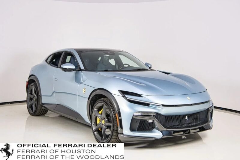 A light blue Ferrari Purosangue SUV with black accents is displayed in a showroom. This best-in-class model features yellow brake calipers and a logo for Ferrari of Houston and The Woodlands, highlighting exclusive SUVs for sale.