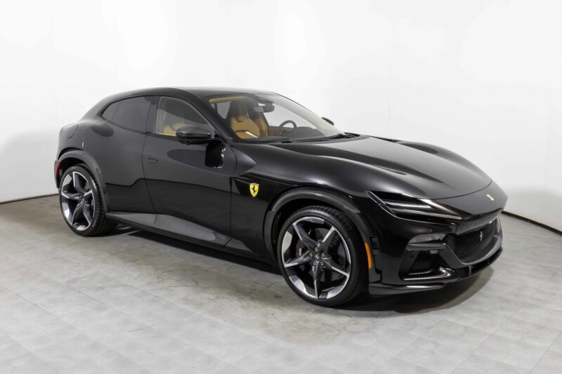 A black Ferrari SUV with a tan interior, a true standout among exotic cars, is parked on a light-colored tiled floor against a plain white background.
