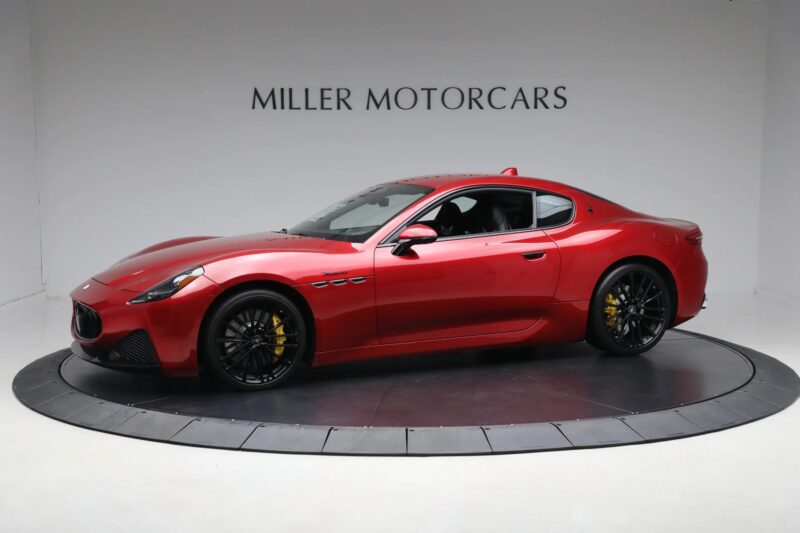 A red Maserati GranTurismo coupe, epitomizing Italian luxury, is displayed in a showroom with a "Miller Motorcars" sign on the wall behind it.