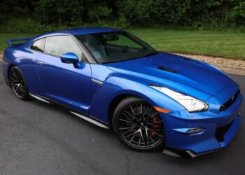 A blue luxury car parked on a paved surface near grass and trees, viewed from the front left side—a stunning choice for those browsing exotic cars for sale.