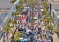 A large crowd gathers on a palm-lined street in Beverly Hills, with various cars and a helicopter on display during the June 15 Rodeo Drive Concours d’Elegance outdoor event.