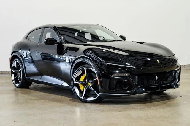 A black Ferrari sports car with yellow brake calipers is parked indoors on a light concrete floor against a plain white wall, perfectly showcasing why it’s considered among the best Ferrari models—alongside the impressive Ferrari Purosangue SUVs for sale.
