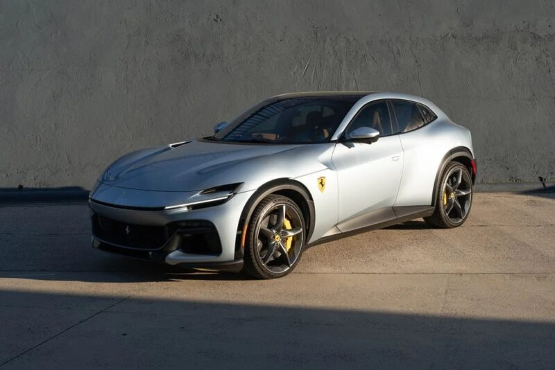 A silver Ferrari Purosangue SUV parked on a concrete surface in front of a plain gray wall, showcasing why it stands out among the best Ferrari SUVs for sale.