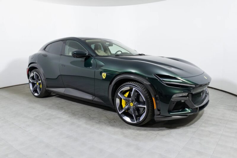 A dark green Ferrari Purosangue SUV is parked in a white indoor studio, showing its front and side profile with yellow brake calipers and the Ferrari logo on the door—a standout among SUVs for sale.