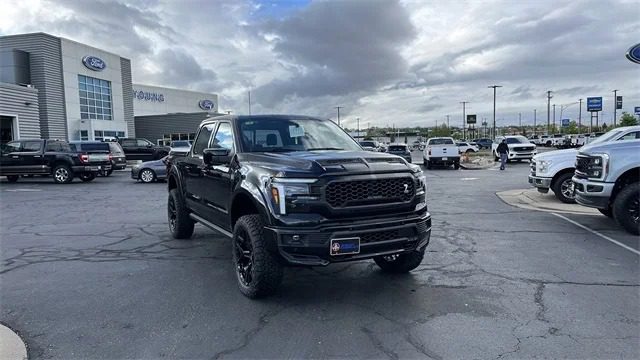 A black Ford F-150 is parked in a dealership lot, surrounded by other vehicles under a cloudy sky, and is currently for sale.