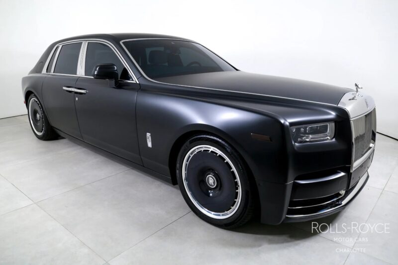 A quintessential black Rolls-Royce Phantom luxury sedan with tinted windows and silver trim is parked indoors on a light-colored floor.