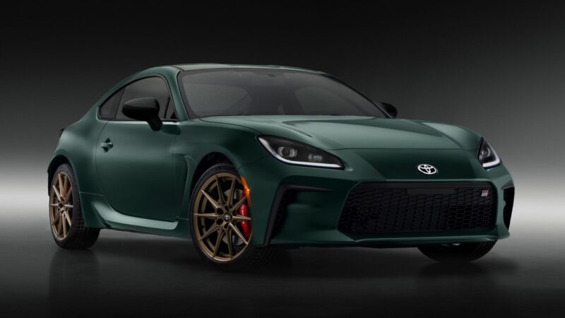 A green Toyota sports coupe, For Sale: Best Sports Car Under $100k, with gold wheels and red brake calipers is parked in a studio with a dark gradient background.