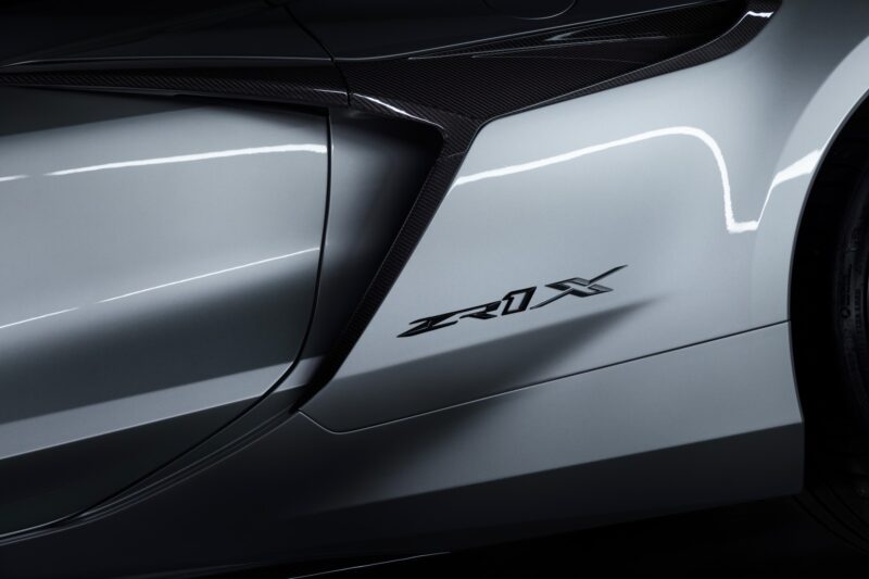 Close-up of a silver car's side panel, featuring a "ZR1X" badge and visible carbon fiber detailing near the door. Revealed: 2026 Corvette ZR1X is the most powerful Chevrolet ever built.