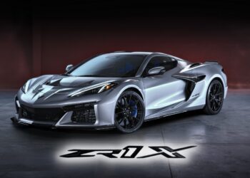 A silver Chevrolet Corvette ZR1 sports car is parked indoors, its model name "ZR1X" illuminated on the floor in front. Revealed: 2026 Corvette ZR1X is the most powerful Chevrolet ever built.
